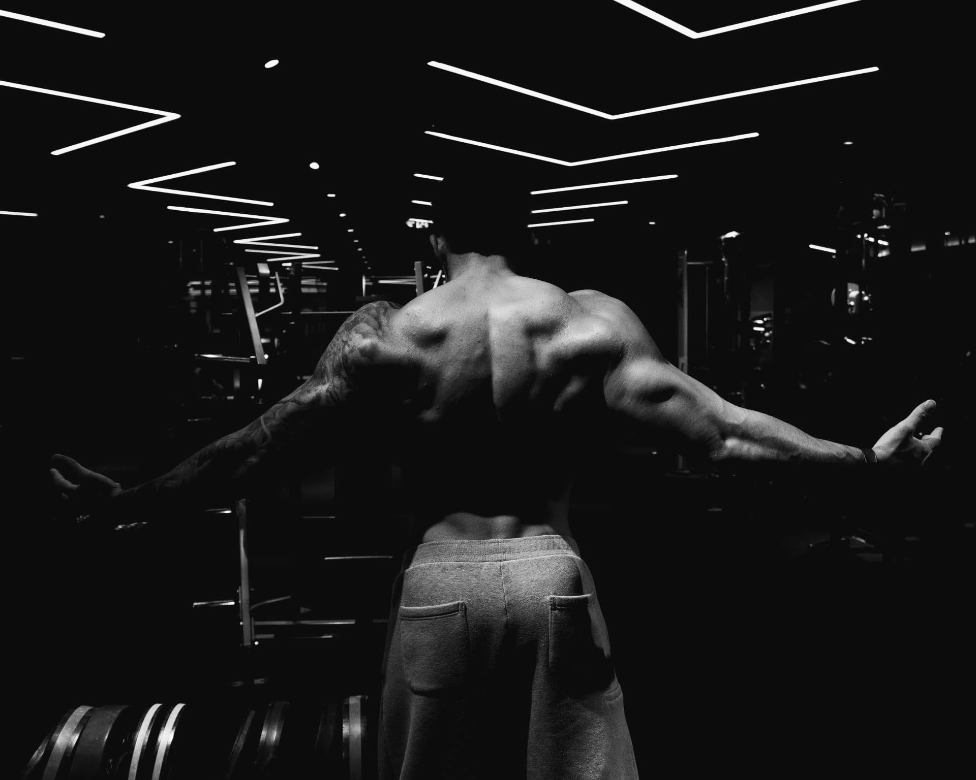 Craig O’Meara standing in the gym with his back to camera and arms wide, photographed in black and white